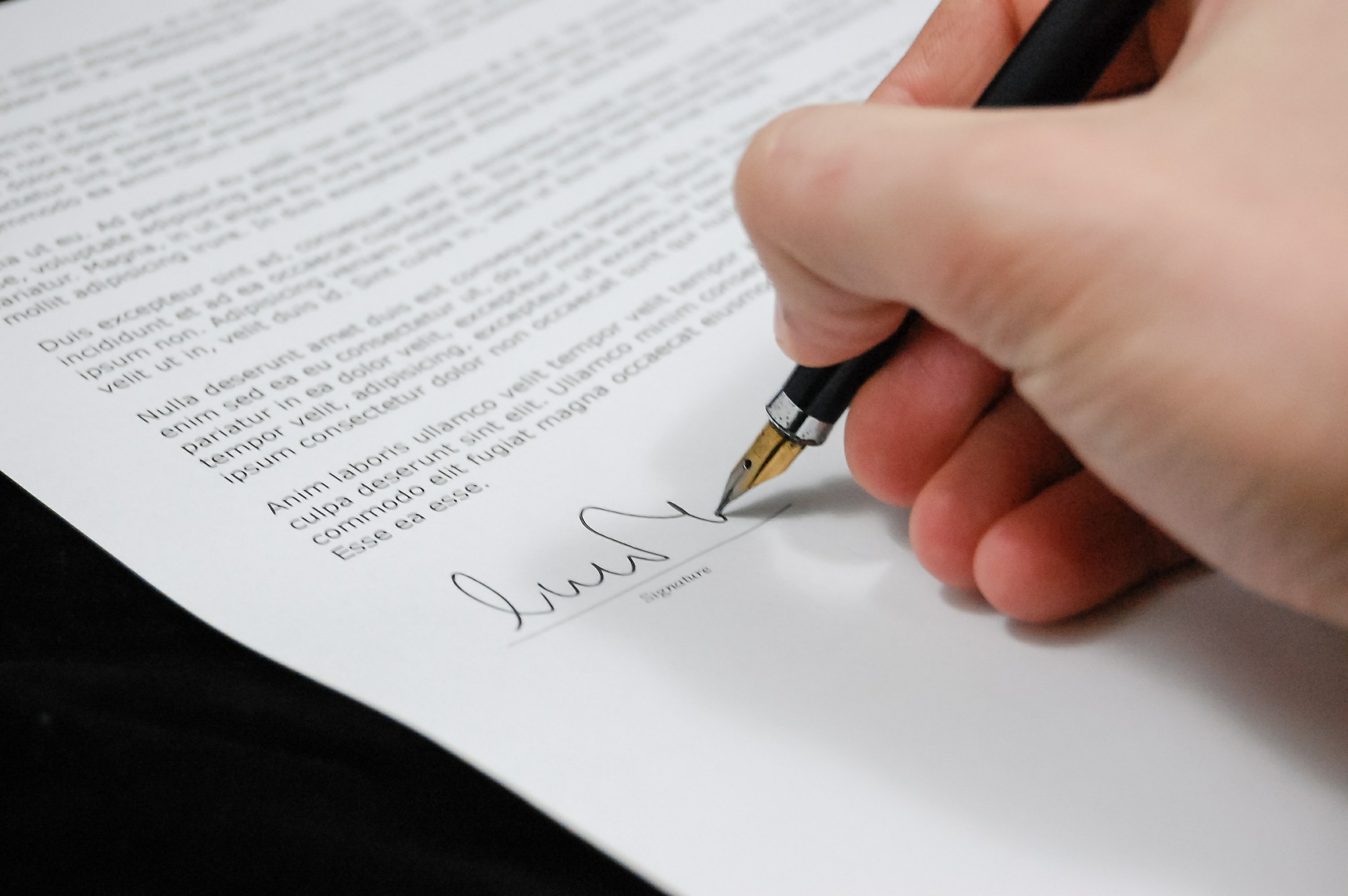 Mano con bolígrafo firmando un documento de papel
